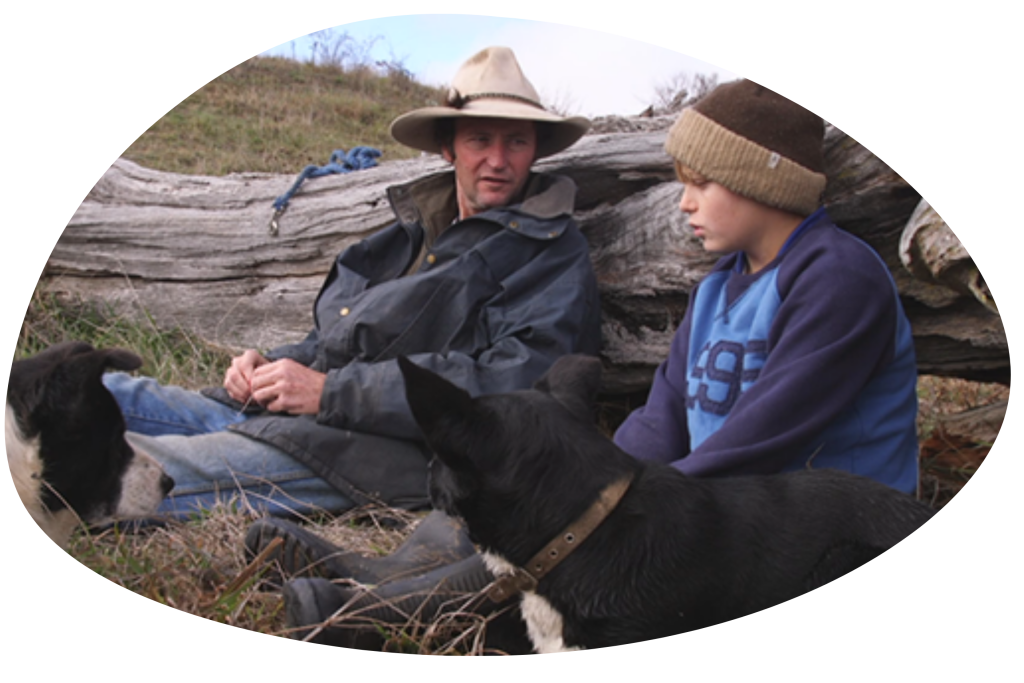 A man, a boy and a dog sitting on the ground against a fallen tree from the documentary Backtrack Boys.