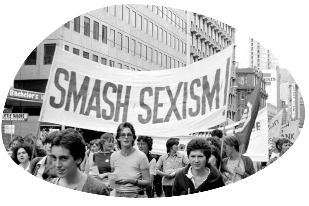 A black and white photo of a protest with a sign saying Smash Sexism.