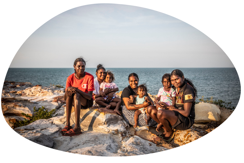 A group of Indigenous children sitting on a cliff with the ocean behind them.